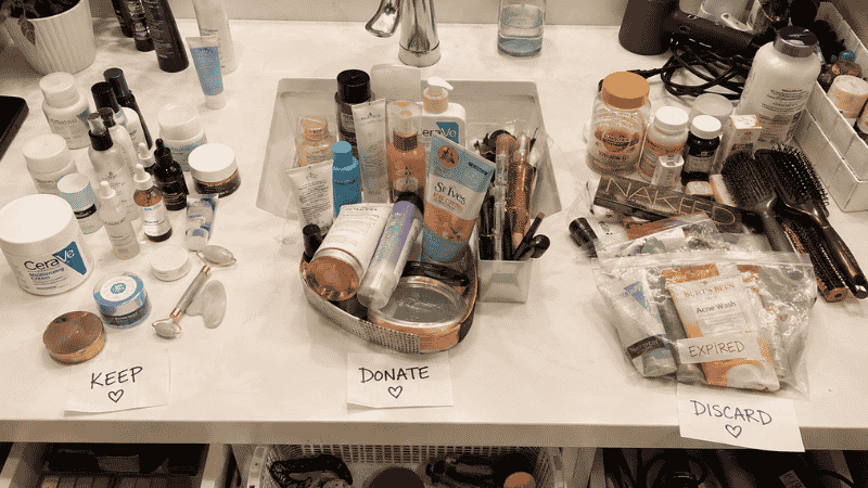 Bathroom counter with all products pulled out sorted into keep donate and discard piles during declutter