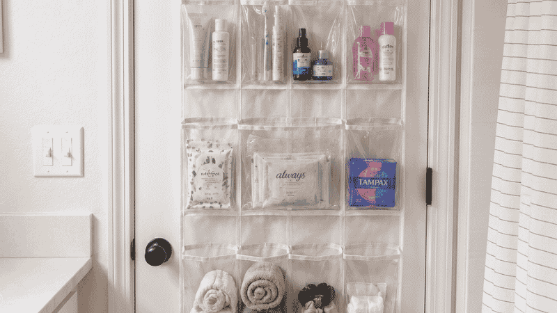 Back of bathroom door with clear pocket over-door organizer holding hair tools toiletries and towels
