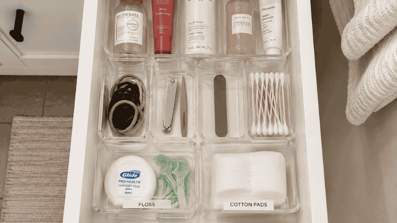 Bathroom vanity drawer organized with clear acrylic dividers creating daily grooming and backup zones