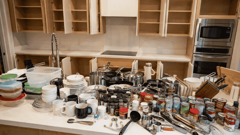 All kitchen cabinet contents laid out on counter for sorting with empty cabinets visible in background