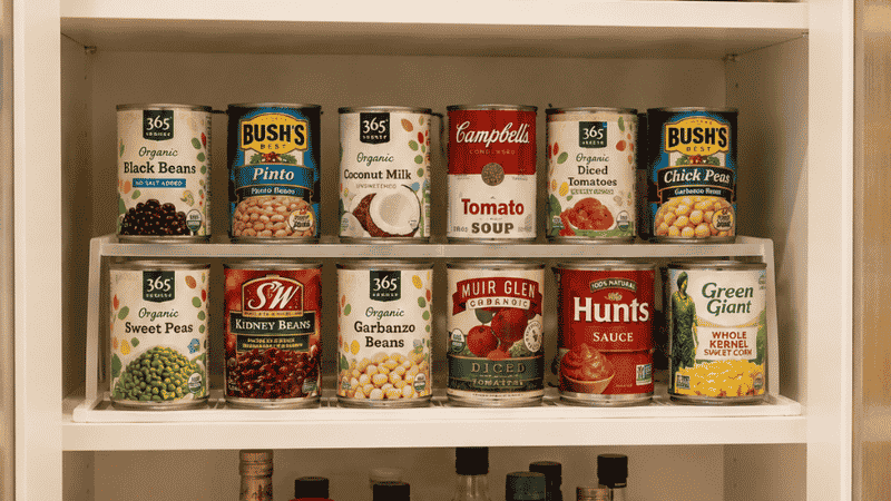 Kitchen pantry cabinet with three shelf levels showing glass canisters canned goods on riser and turntable for bottles