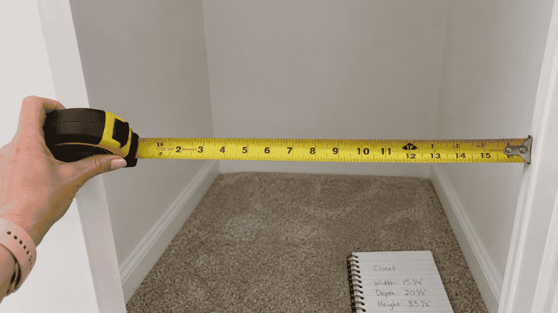 Hand measuring interior width of empty small closet with tape measure before buying organizers