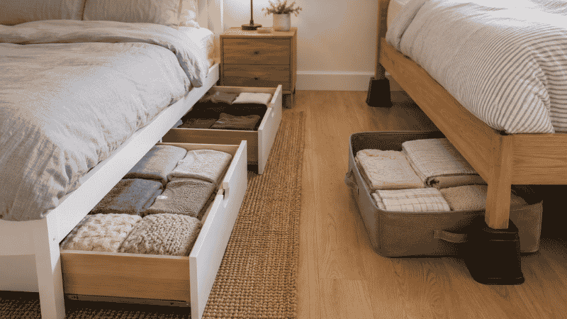 Small bedroom showing storage bed frame with open drawers and under-bed flat storage bins pulled out