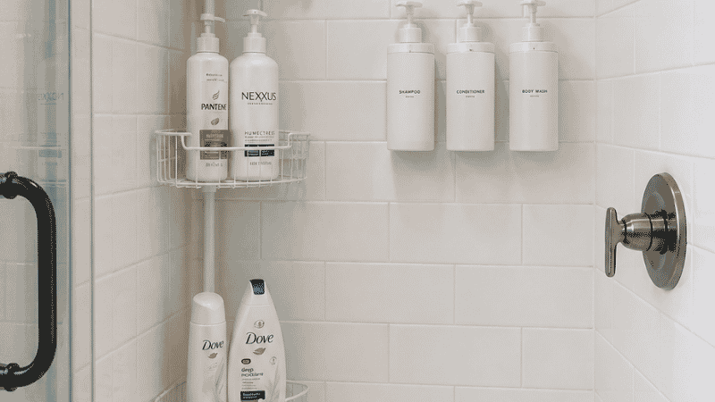 Small shower organized with tension pole caddy and wall mounted pump dispensers replacing loose bottles