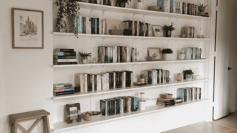 Small apartment living room with floor to ceiling floating shelves using full vertical wall space for storage