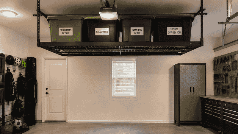 Garage ceiling mounted overhead storage rack holding four labeled seasonal bins for holiday decor and camping gear