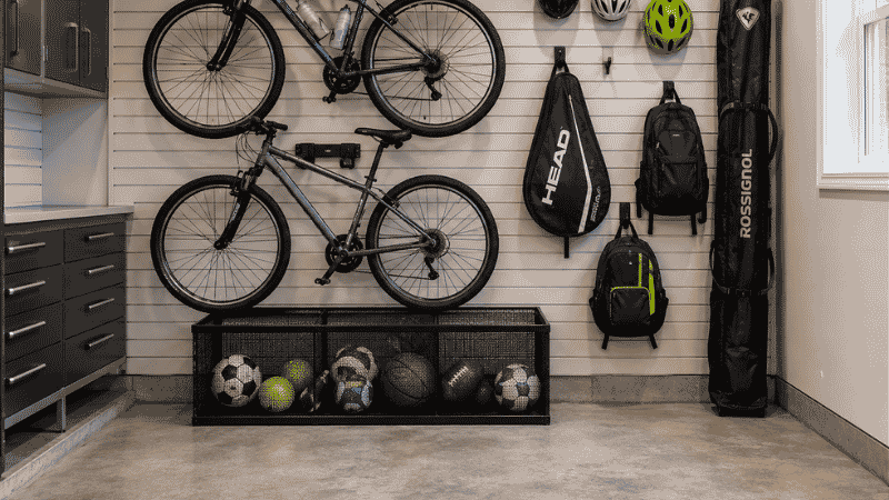Garage sports zone with two bikes on wall hooks ball bin below and helmet hooks with clear floor space