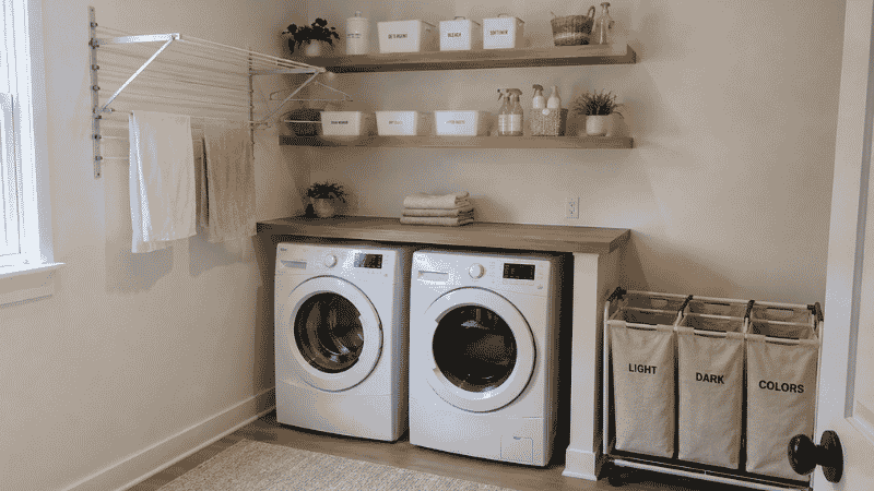 Organized laundry room showing folding counter above machines floating shelves drying rack and sorting hampers