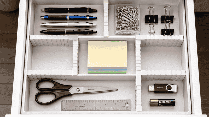 Desk drawer organized with expandable divider showing separate compartments for pens clips sticky notes scissors and small items