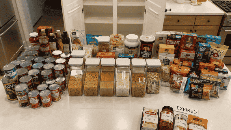 All pantry contents laid out on kitchen counter grouped by category during audit with expired items set aside