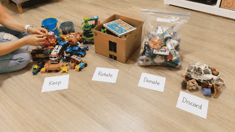 Toy audit in progress showing four piles on floor labeled keep rotate donate and discard