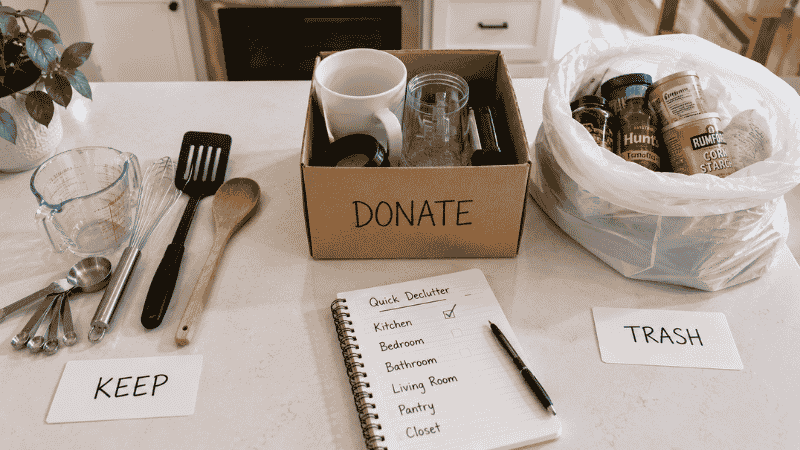 Kitchen declutter checklist in progress showing three sorted groups keep donate and discard with handwritten checklist showing rooms completed