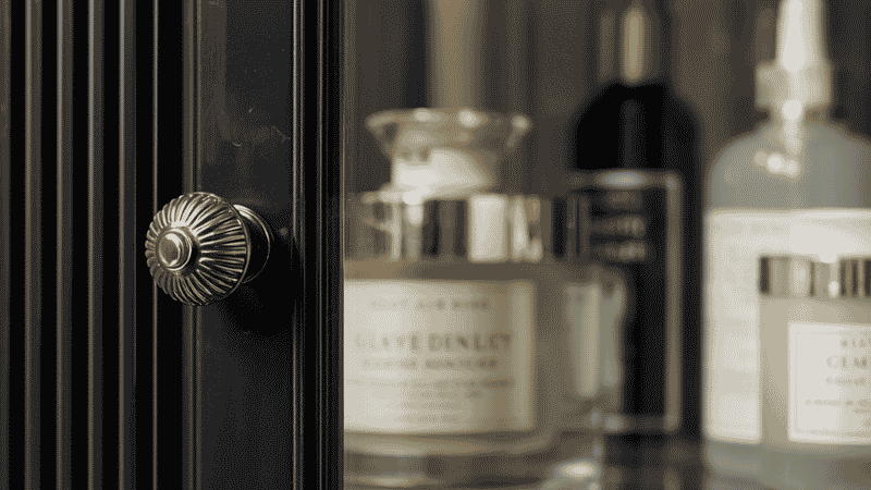 A close-up detail shot of a reeded glass cabinet door blurring the shapes of luxury apothecary jars and skincare bottles inside.